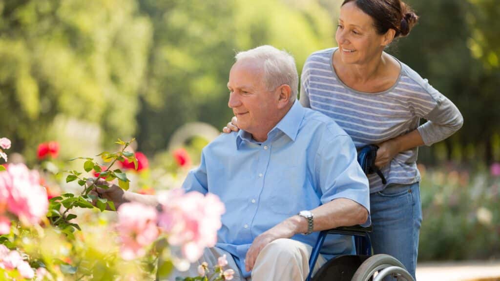 An elderly man in a wheelchair enjoys a sunny day in the garden