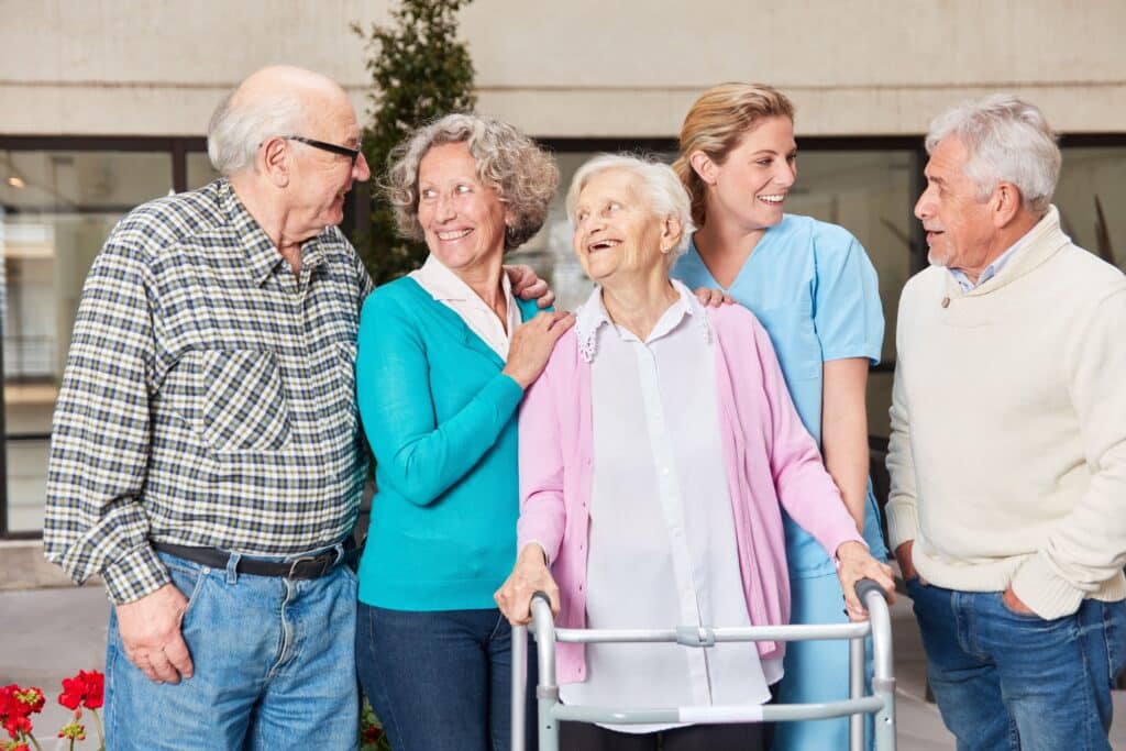A group of elderly people gathers around a woman using a walker
