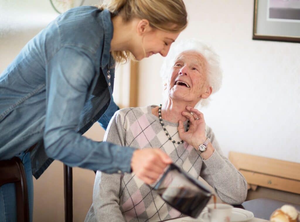 A woman assists an older woman as she pours her coffee