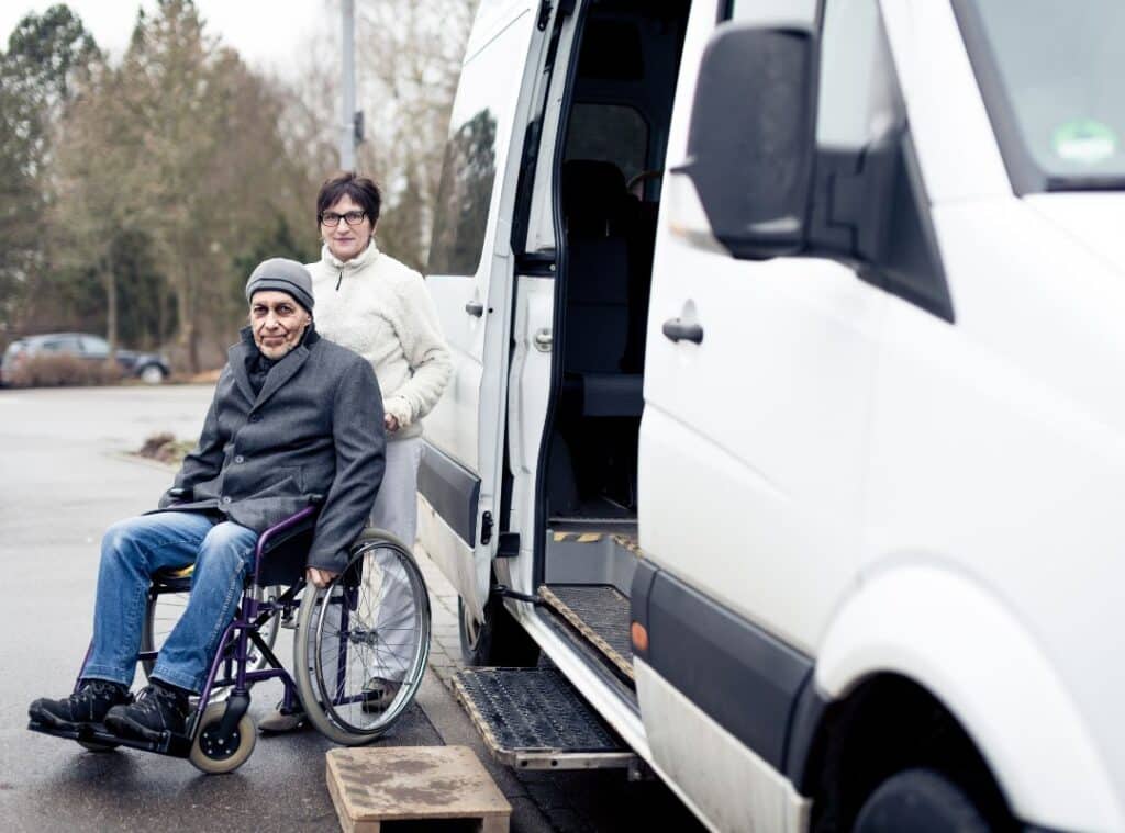 Elderly man in wheelchair with transportation van beside of them